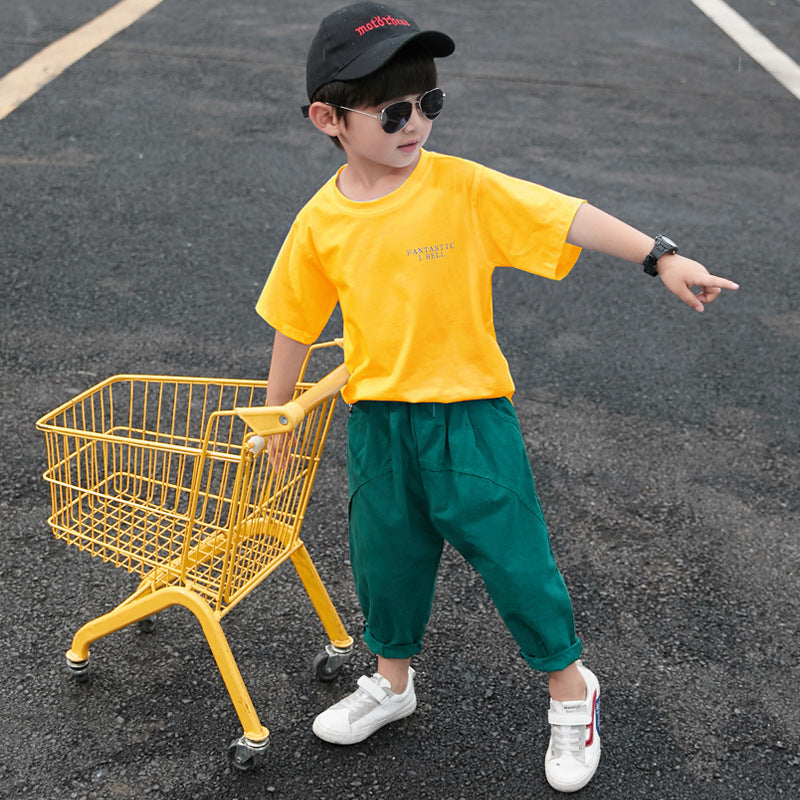 A child wearing a white short-sleeve shirt with a cartoon dinosaur print and green pants, walking away from the camera.