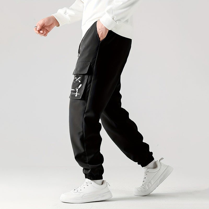 A person wearing black straight-leg ankle-tied overalls casual pants with a mid-waist waist and white sneakers.