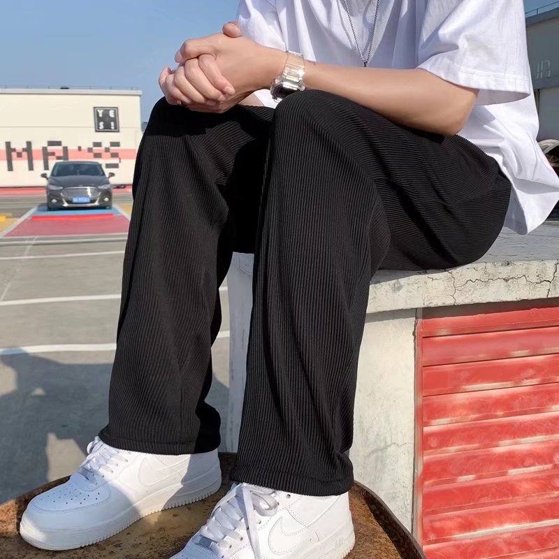 A man wearing black striped ice silk leggings and a white t-shirt, standing in front of a wall with 'FRIENDS' themed decorations.