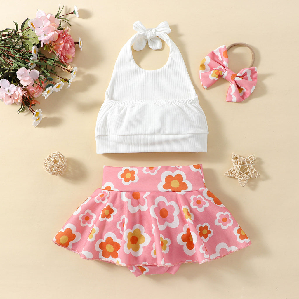 A set of children's clothing including a white sleeveless top with a bow at the neck, a pink skort with a floral pattern, and a matching hairband, displayed against a beige background with decorative elements like flowers and stars.