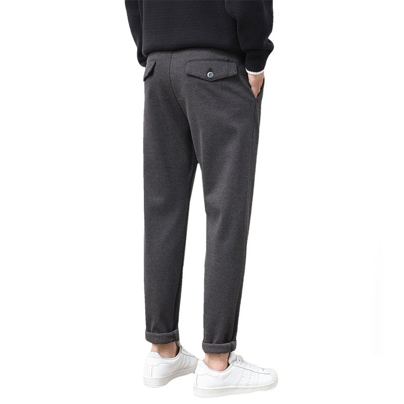 A pair of men's straight-leg casual pants in dark gray color, displayed on a model wearing white sneakers and a black top.