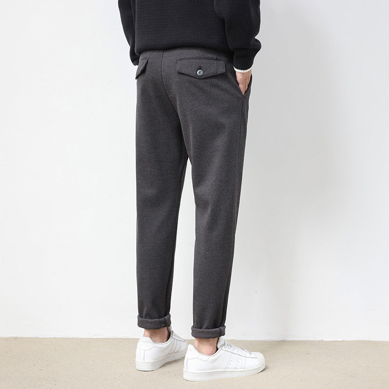 A pair of men's straight-leg casual pants in dark gray color, displayed on a model wearing white sneakers and a black top.