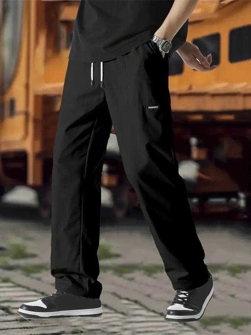 A pair of men's casual pants in green color, displayed on a model against a street backdrop.